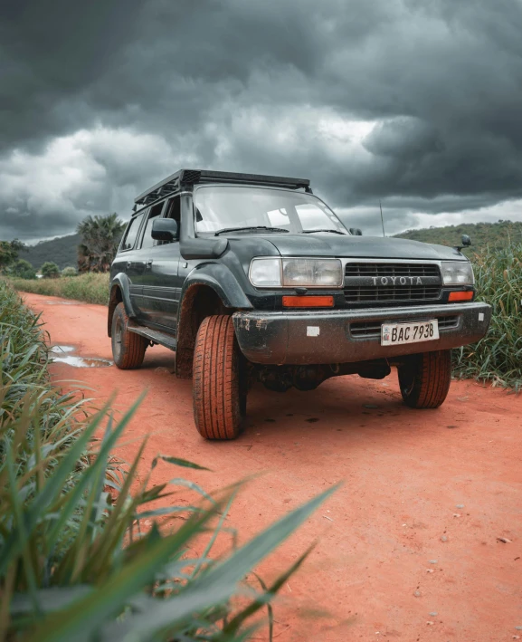 a truck parked next to a red dirt road under a stormy sky