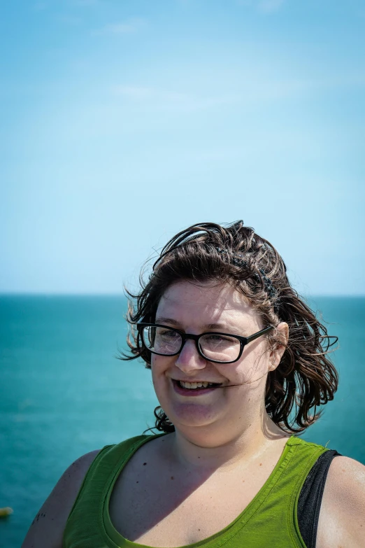 a woman smiling and wearing glasses standing in front of an ocean