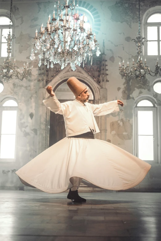 a man in a white tuxedo dancing with his arms spread out and a chandelier hanging overhead