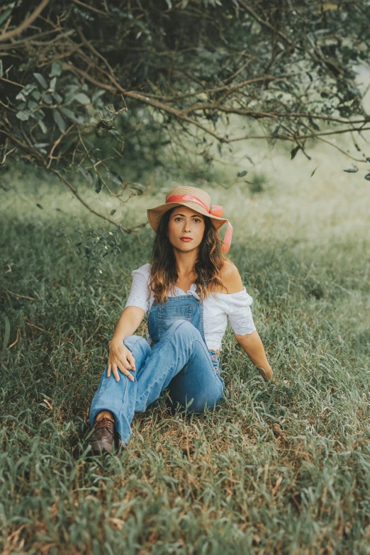 a beautiful young lady sitting in a field by a tree