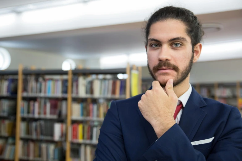 a man standing in front of a bookshelf wearing a suit and tie