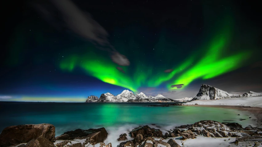 an aurora lights up the night sky above the mountains near water