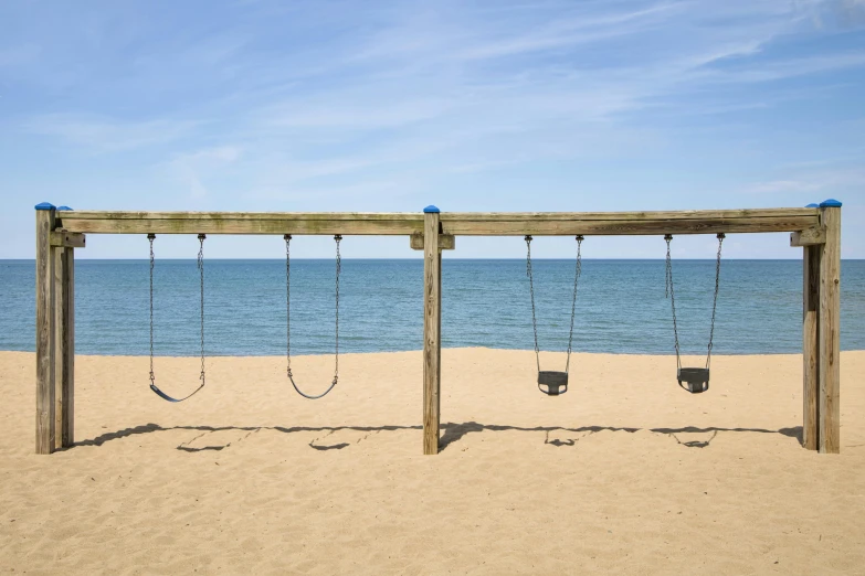 a row of swings at the beach with an ocean view in the background