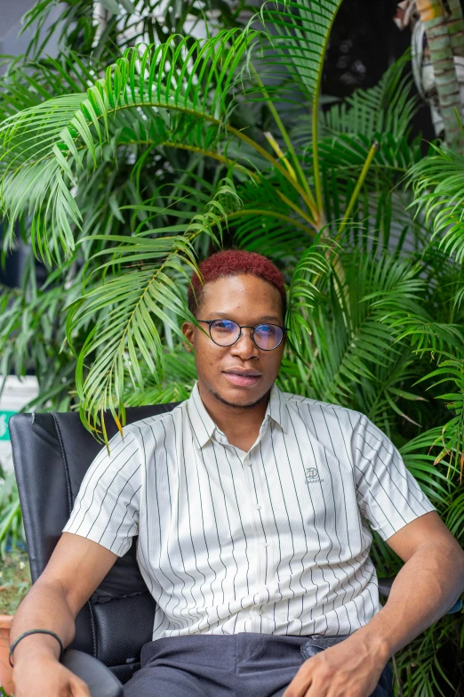 an african american male sitting in a chair, wearing glasses