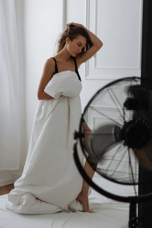 a woman in white dress standing in front of a fan