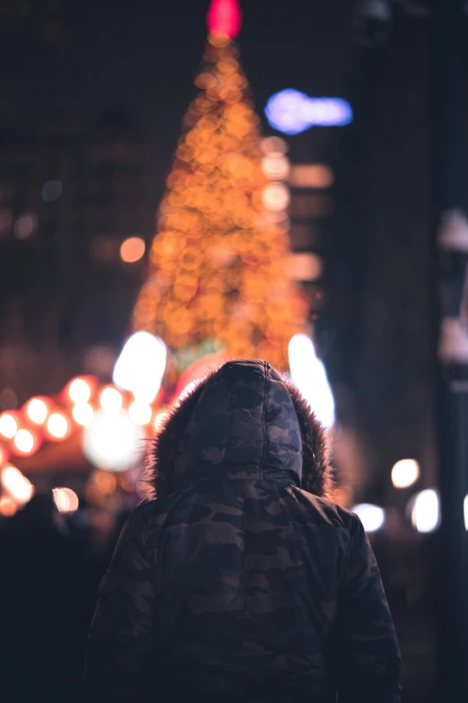 person looking up at lighted christmas tree in city at night