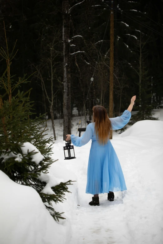 a girl in a blue dress holding a lantern in the snow