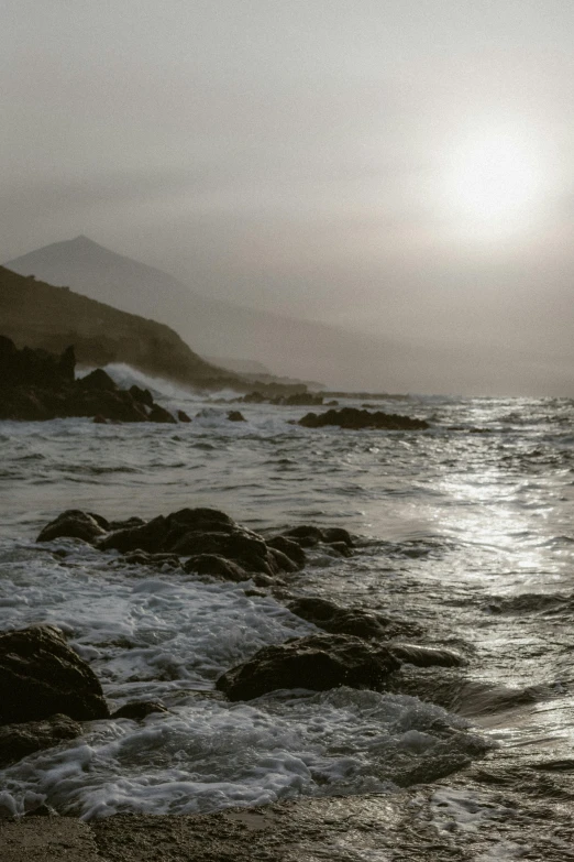 the sun shining over the ocean and rocky shore