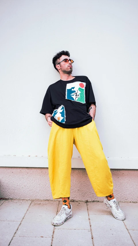 a man posing with his foot on the ground in a black shirt and yellow pants