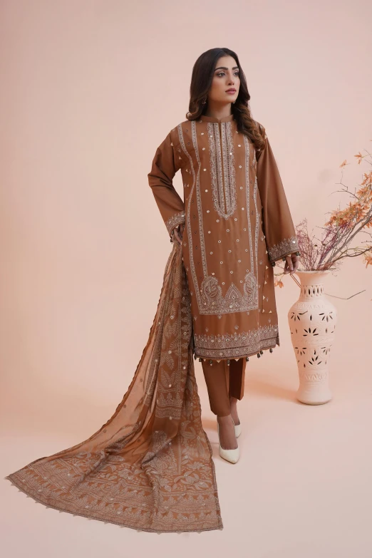 a woman wearing brown attire standing in front of a vase