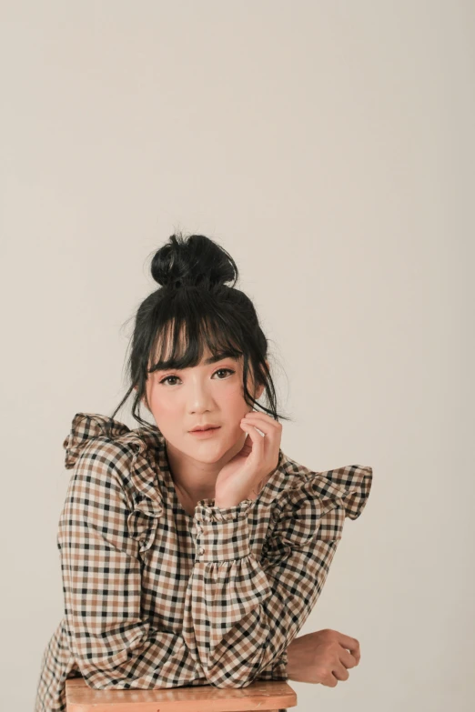 a woman in plaid shirt sitting at a table with her hand on her cheek