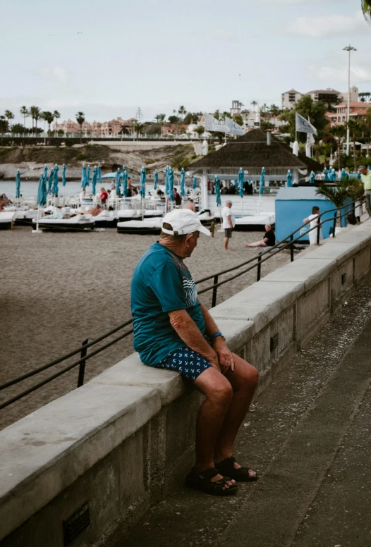 an elderly man sits on a concrete wall looking at boats docked