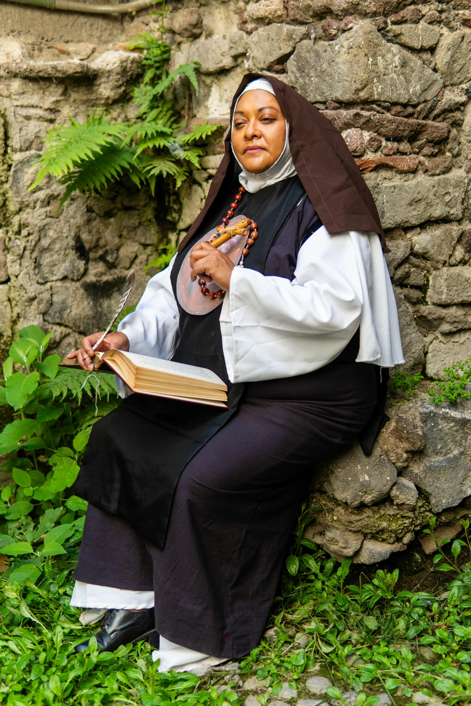 a nun sitting on some rocks with an open book