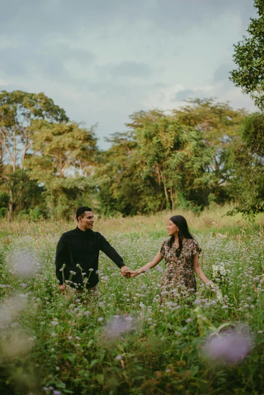 an engaged couple hold hands while walking through a field of wildflowers