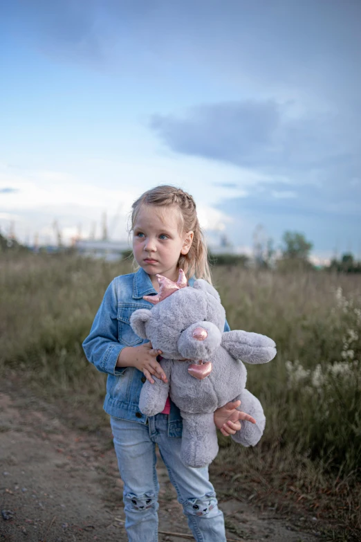 girl holding stuffed toy animal in field by grass