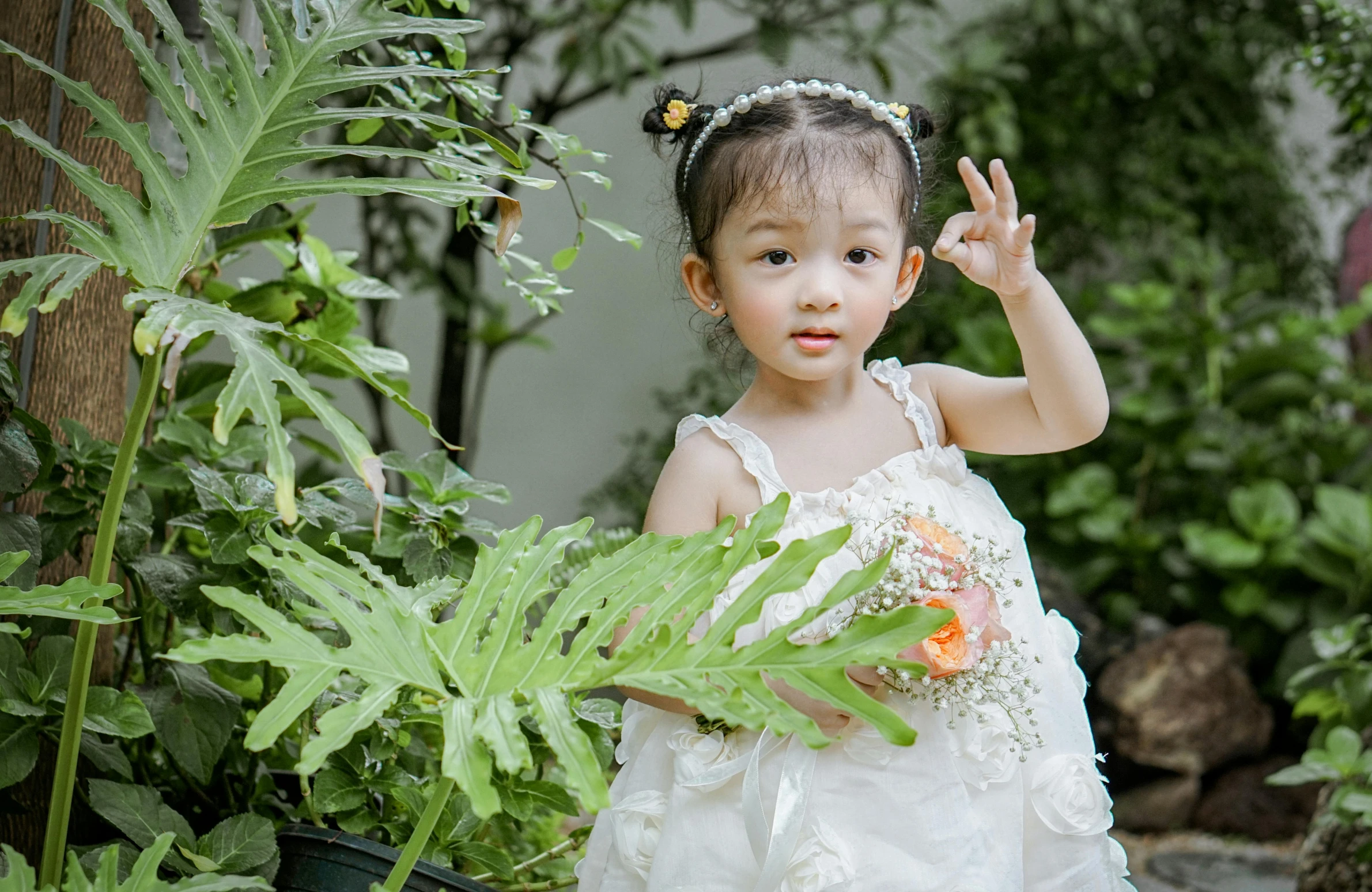 little girl in white dress holding plants and waving her finger