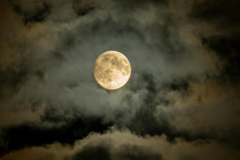 a bright yellow moon rises through clouds against the dark sky