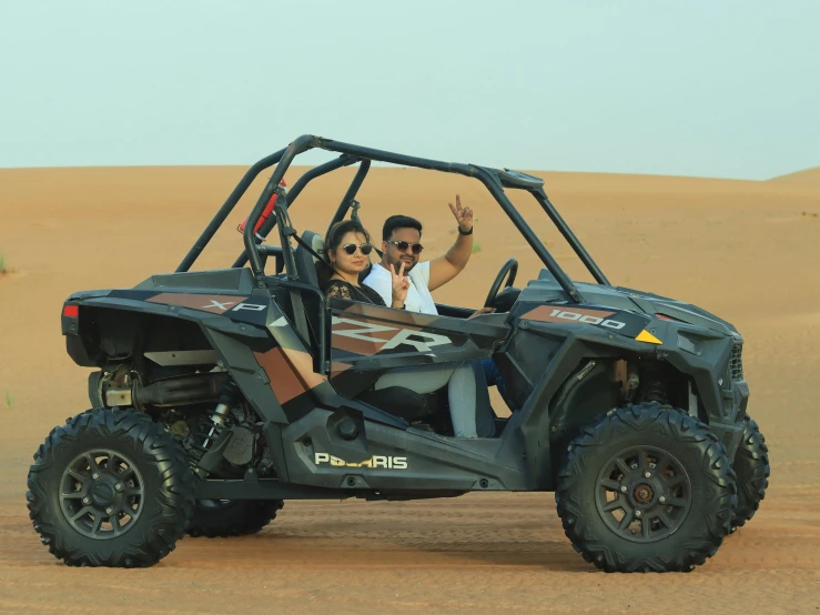 a man and a woman in a gray atv going through the sand