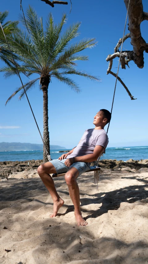 a man is sitting in a hammock on the beach