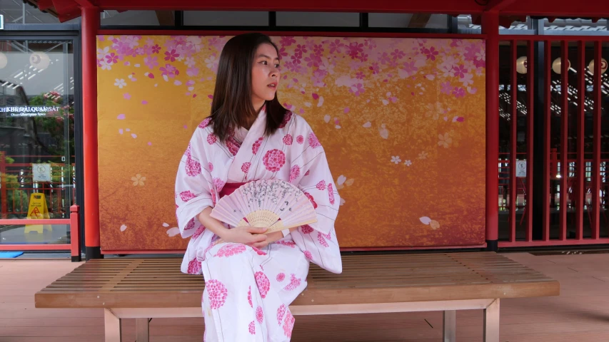 the woman sits on a bench and is dressed in traditional japanese clothes