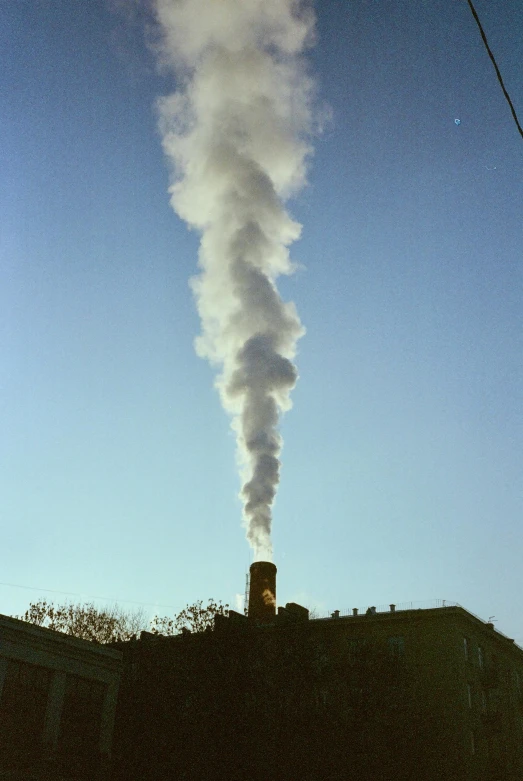 a train emits steam in the air and over the top of some buildings
