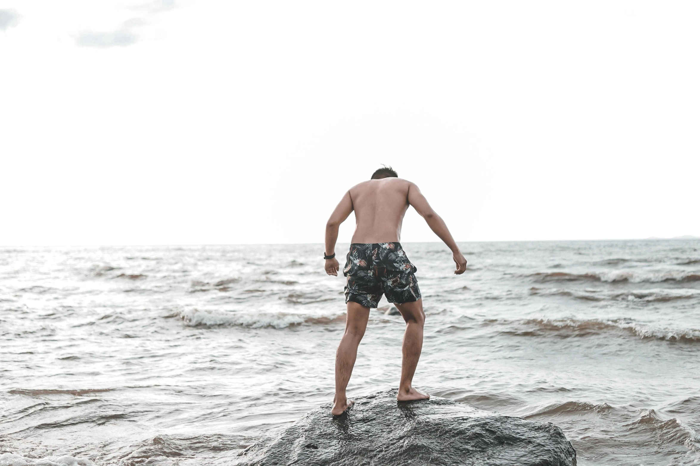 a shirtless man standing on a rock looking out at the ocean