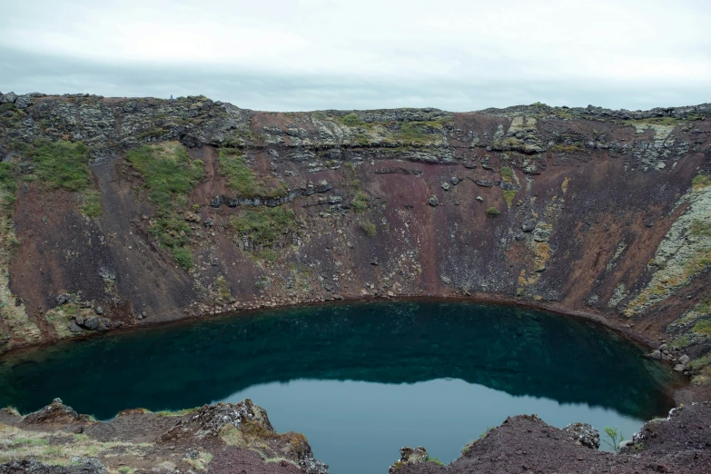 a huge crater sits near a lake with green water