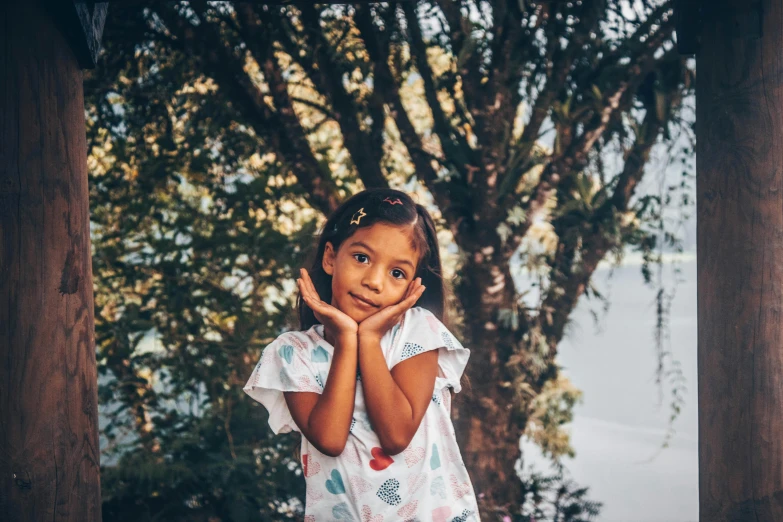 a little girl standing under a tree with her hands together