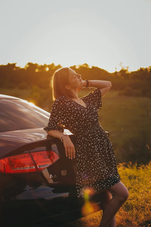 a woman in a dress stands next to a car