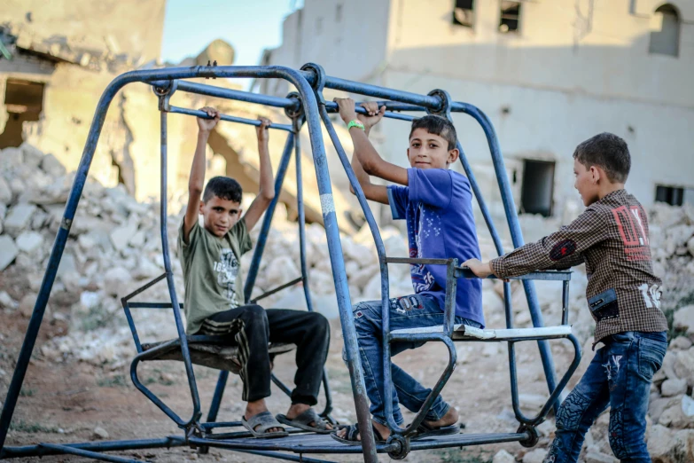 children ride on the swings in a destroyed out - building area