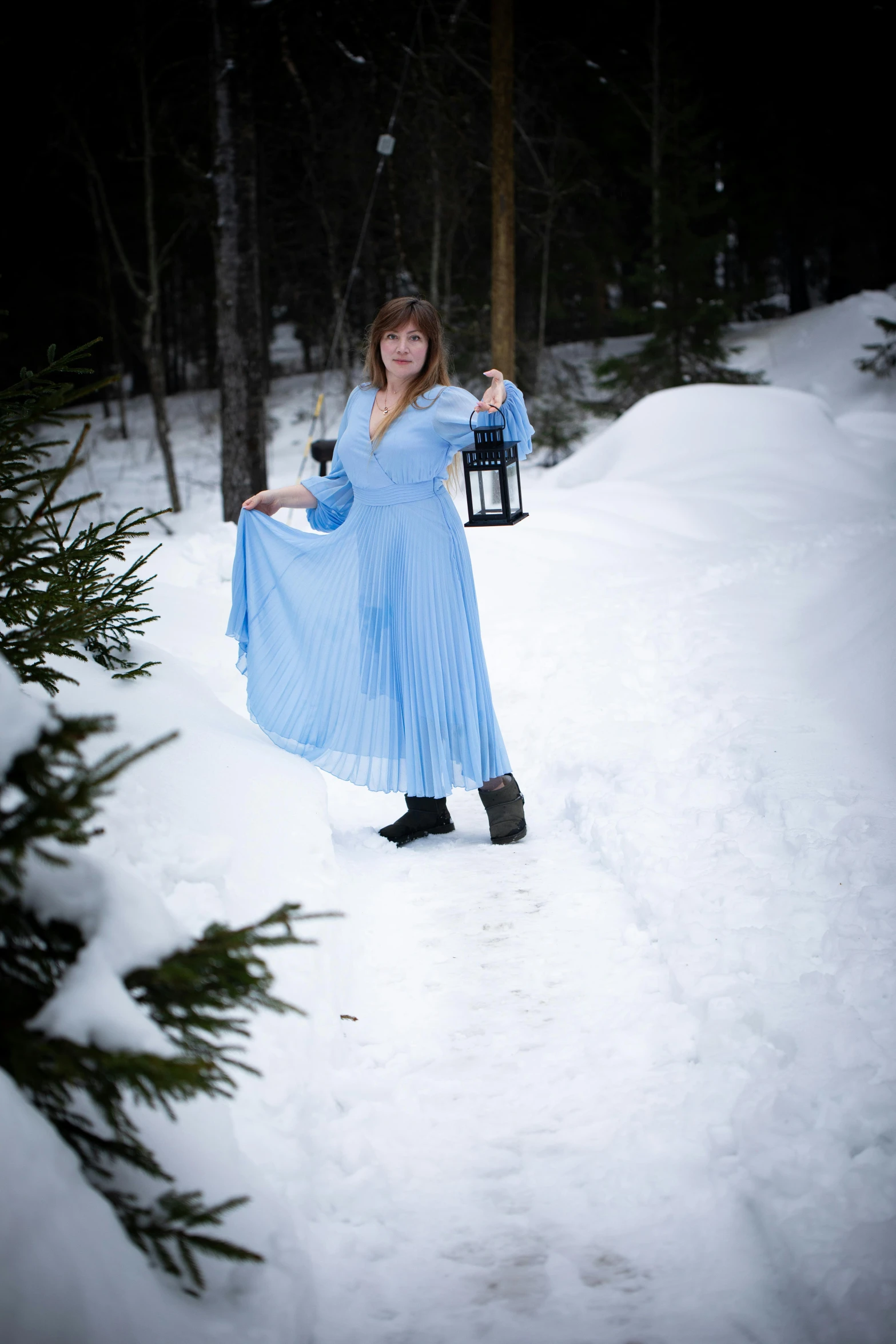 a woman wearing a blue dress and holding a lantern standing in a snowy forest