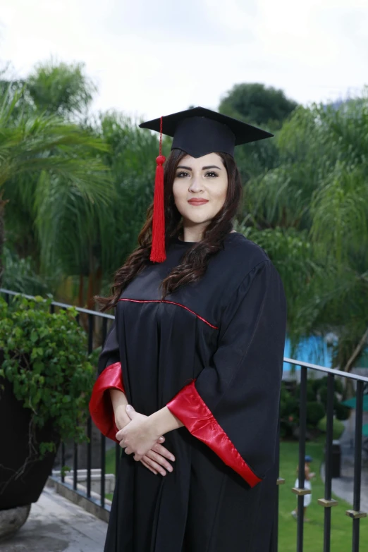 a woman in graduation robes, standing near a fence