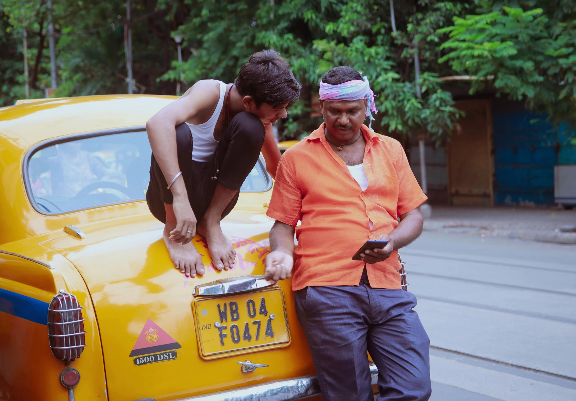 two men stand next to an old yellow car