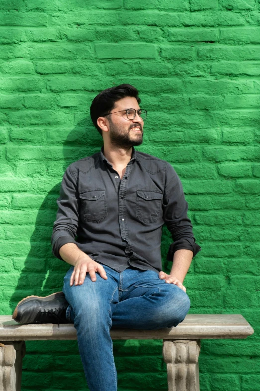 a man sitting on top of a bench next to a green wall