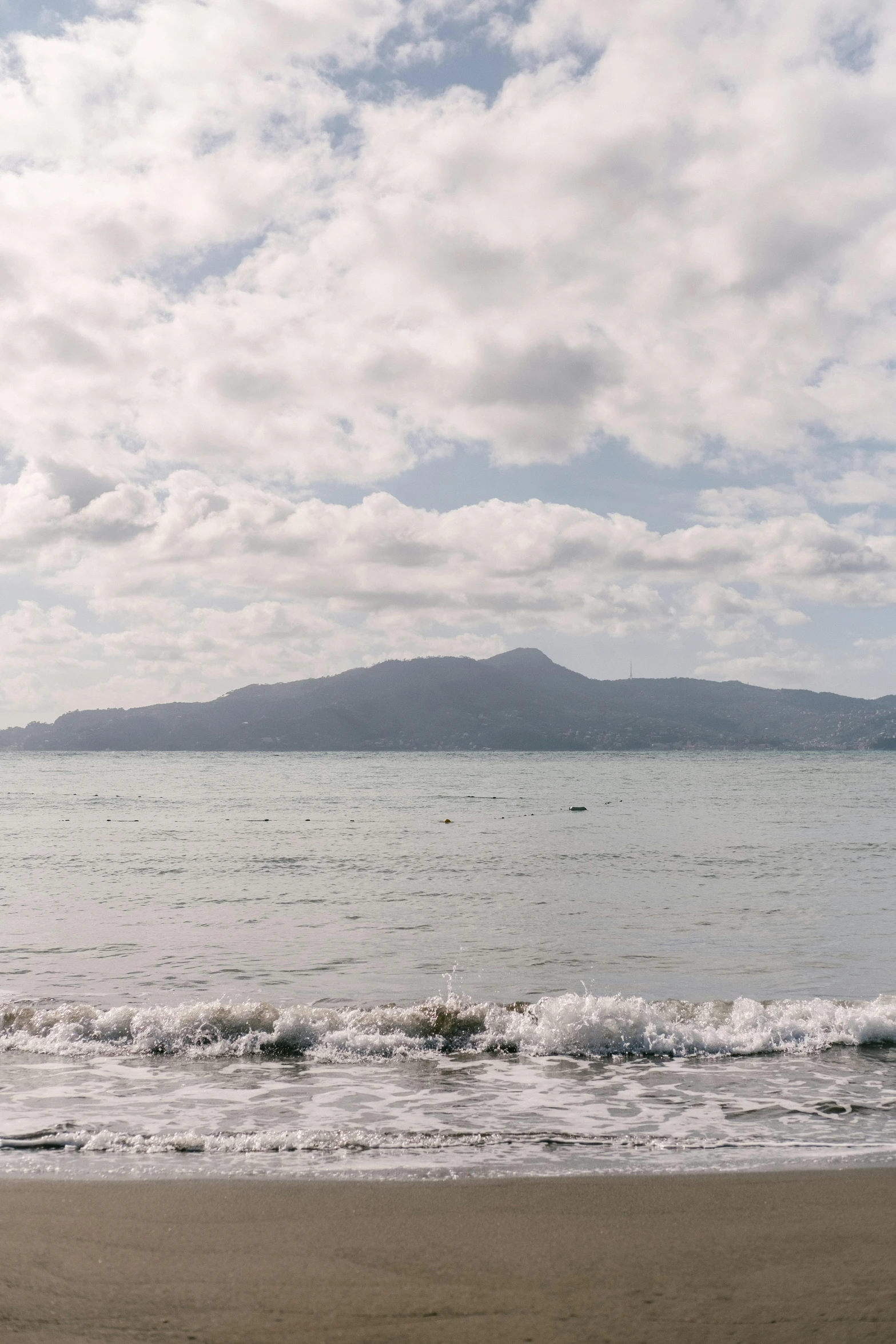 an ocean beach with low hills and cloudy skies