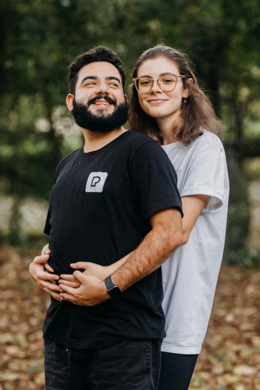 a smiling couple standing on a path surrounded by fall leaves