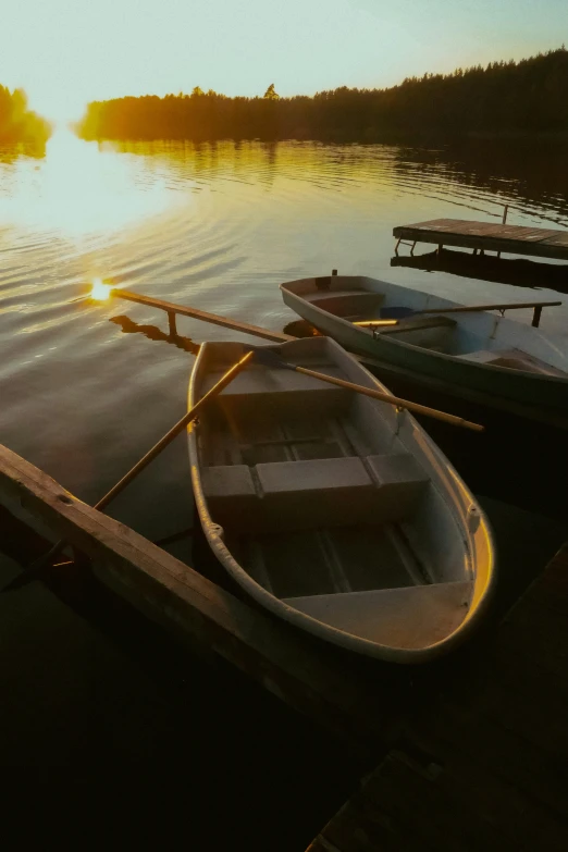 two wooden boats tied to a dock during the sun sets