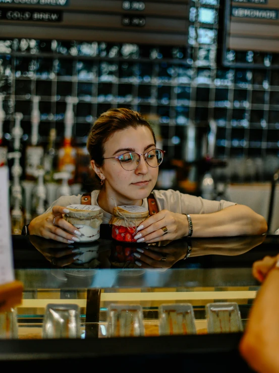 a girl with glasses holding coffee while sitting in a bar