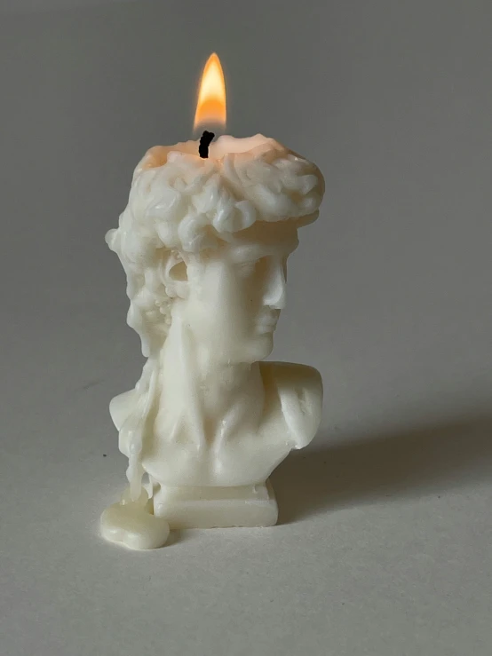 a lit candle with the head of a man carved to look like a human head