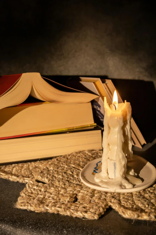 a lit candle on top of a plate next to books