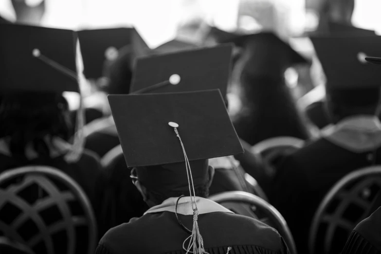 graduates wearing caps and gowns sit at commencement