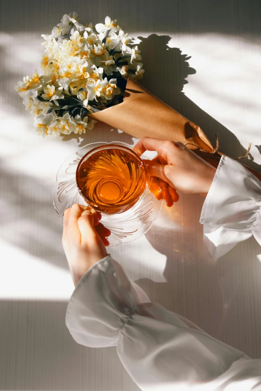 a woman holding a cup filled with tea near flowers