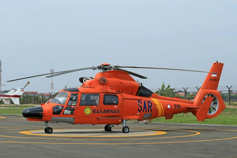 an orange and white helicopter on runway next to grass