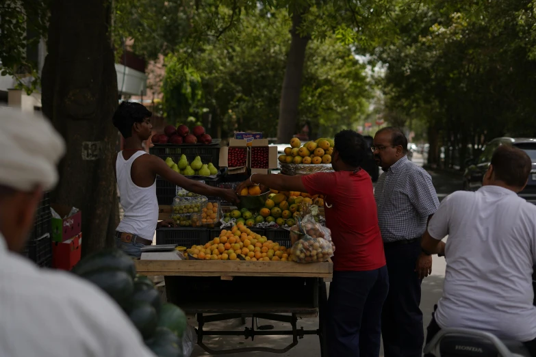 people are standing around the fruit vendor at the market