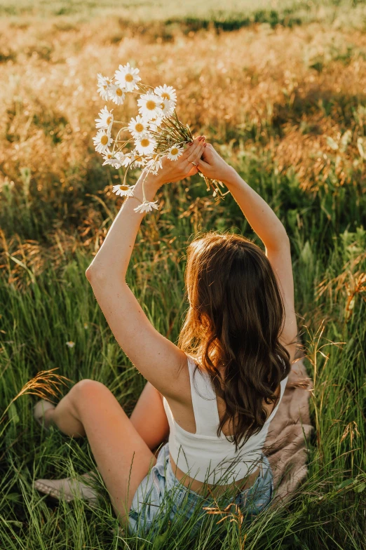 a woman holding a bunch of flowers on top of a field