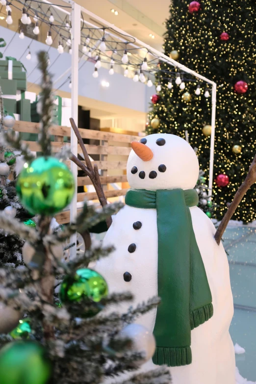 a snow man in a scarf next to a christmas tree