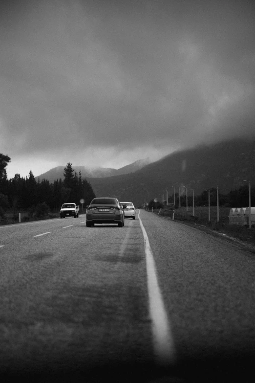 cars driving down a road at dusk in a black and white po