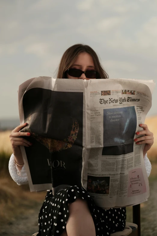 a young lady is sitting and reading a news paper