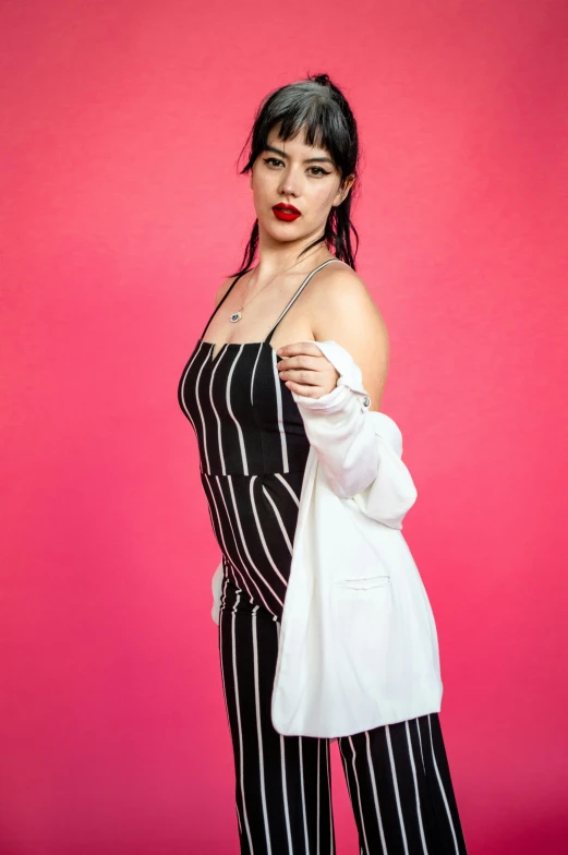 a woman standing against a pink wall wearing striped clothes