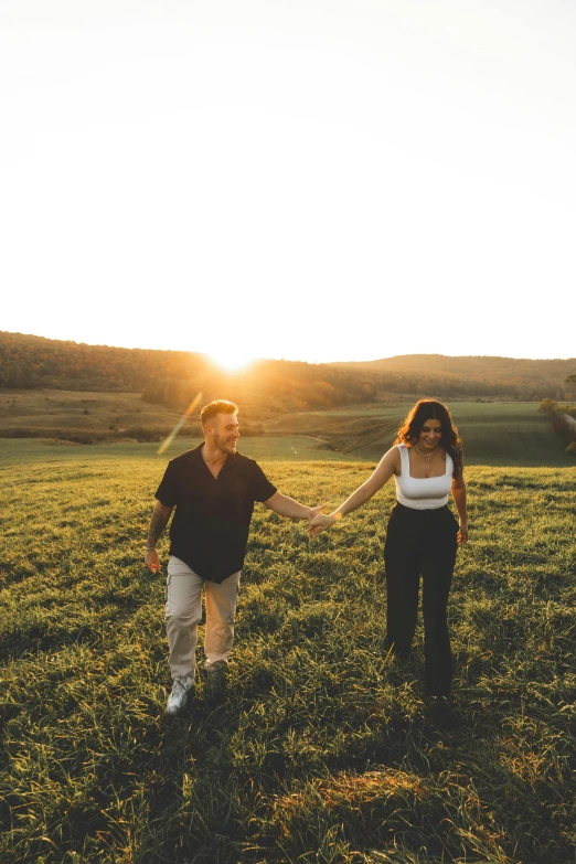 two people holding hands walking across a grass covered field